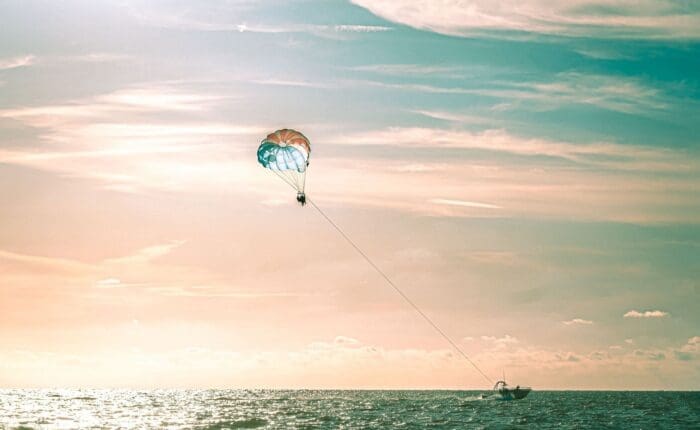 A person parasailing over the ocean, towed by a boat under a pastel sky.