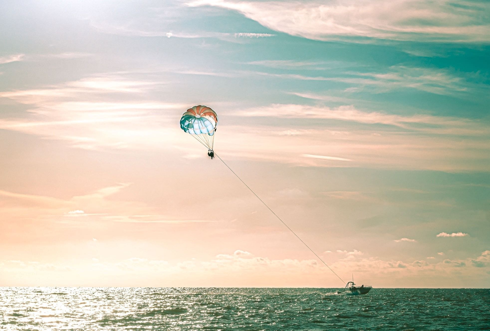 A person parasailing over the ocean, towed by a boat under a pastel sky.